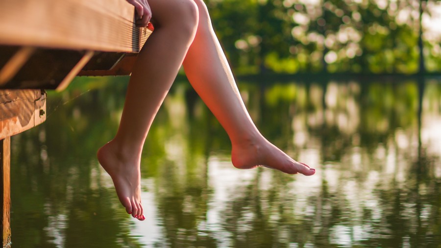 Füße baumeln entspannt über ruhigem Wasser von einem Steg herunter.