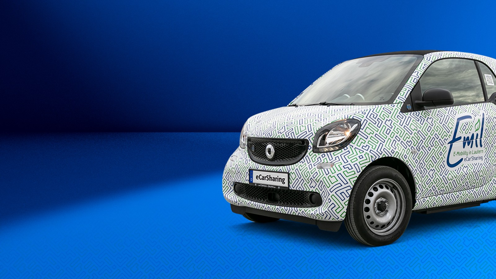 Smart ForTwo mit Emil eCarSharing-Branding auf blauem Hintergrund ragt rechts bis zu Hälfte ins Bild hinein. 