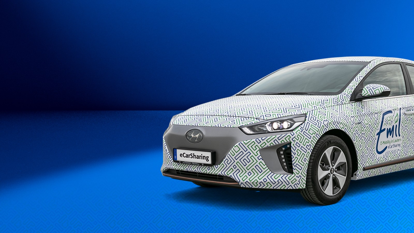 Hyundai IONIQ mit Emil eCarSharing-Branding auf blauem Hintergrund ragt rechts bis zu Hälfte ins Bild hinein. 